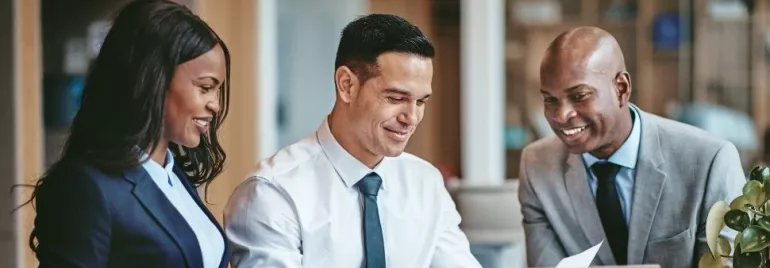 Three people in formal attire smiling at a laptop.