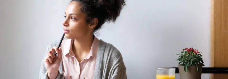 Person sitting at a table with a pen, looking thoughtful.