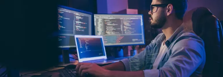 Person programming with multiple screens displaying code.