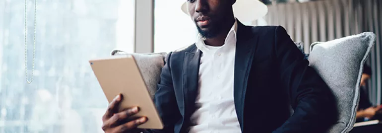Person in a suit reading on a tablet by a window.