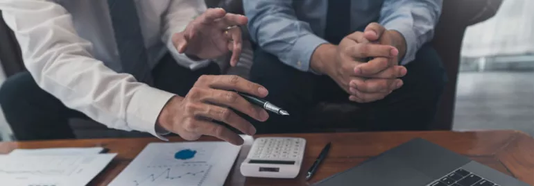 Two people discussing charts and graphs at a table with a laptop.