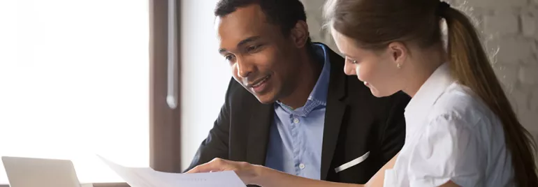Two people reviewing a document at a desk with a laptop.