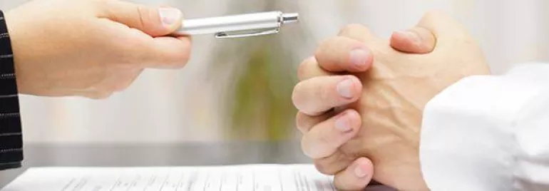 Two people at a table with a document, one holding a pen.