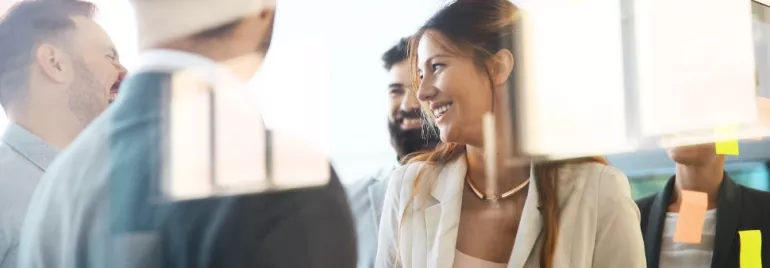 Group of people smiling during a meeting with sticky notes on a window.