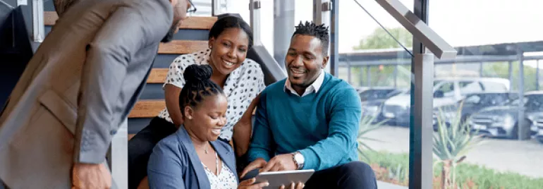 Group of people sitting on stairs looking at a tablet.