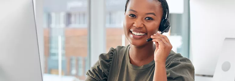 Person smiling at computer with headset in office.