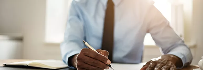 Person writing at a desk with a notebook and pen.