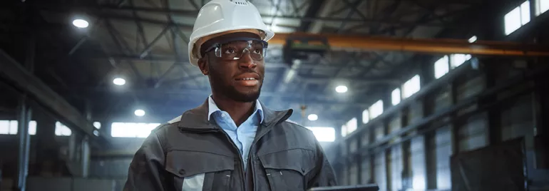 Worker wearing a hard hat and safety glasses in a factory setting.