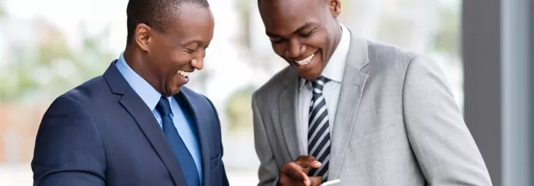 Two people in business attire smiling and looking at a phone.