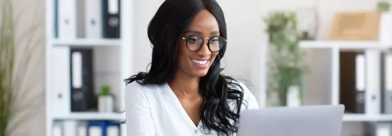 Person smiling while working on a laptop in an office.