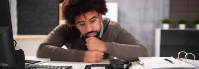 Person at a desk looking thoughtfully at a phone.