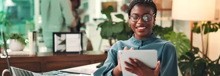 A smilingwoman standing in an office on an ipad 