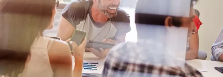 People having a friendly meeting in an office, smiling and using devices.