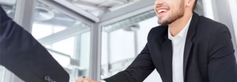 Person in a suit smiling, shaking hands in a modern office.