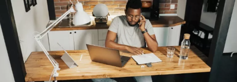 Person on the phone at a wooden desk with a laptop and notebook.