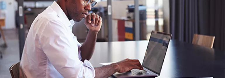 Person working on a laptop at a table with documents.