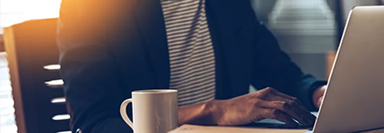 Person working on a laptop with a coffee cup on the desk.