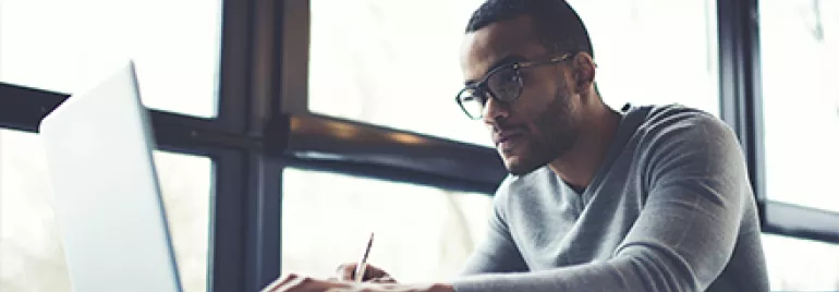 Person working on a laptop at a desk by a large window.