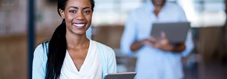 Person smiling while using a tablet, blurred office setting.