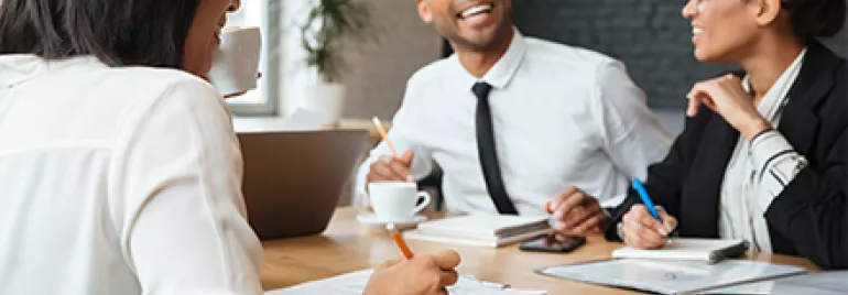 Three people smiling and talking during a meeting in an office setting.