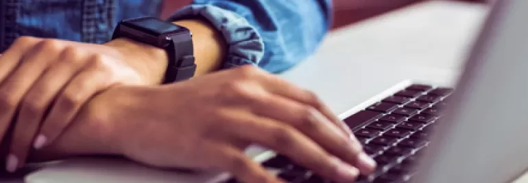 Person typing on a laptop wearing a smartwatch.