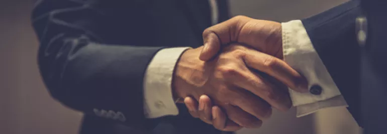 Two people in suits shaking hands indoors.