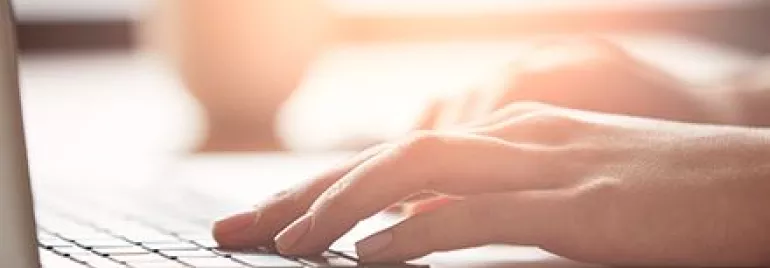 Mains tapant sur un clavier d'ordinateur portable en lumière douce.