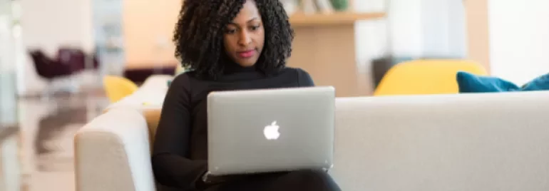 Person sitting on a sofa with a laptop in a bright room.