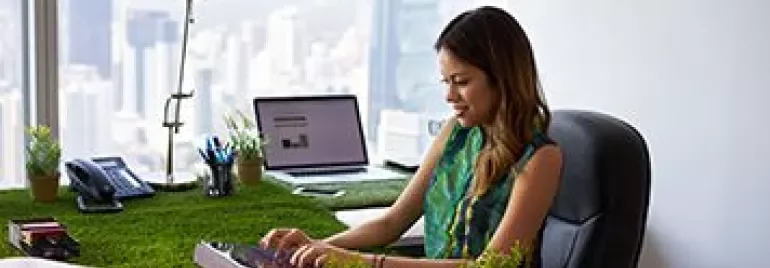Person working at a desk covered in grass with a city view in the background.
