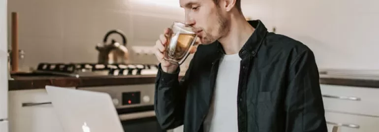Person drinking tea while using a laptop in a kitchen.