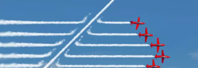 Red planes in formation, one breaking away, leaving white smoke trails against a blue sky.