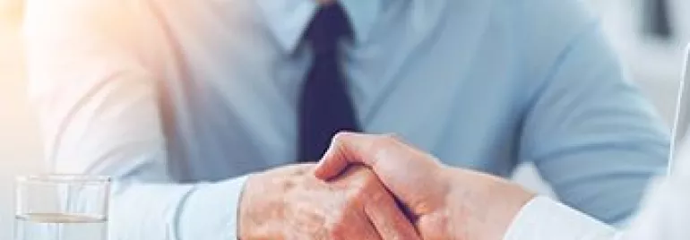 Deux personnes se serrant la main à travers une table dans un bureau ensoleillé.