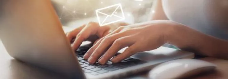 Person typing on a laptop with email icons floating above.