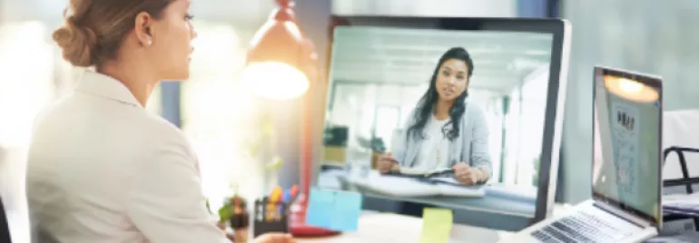 Person using a computer to video call a colleague in a bright office.