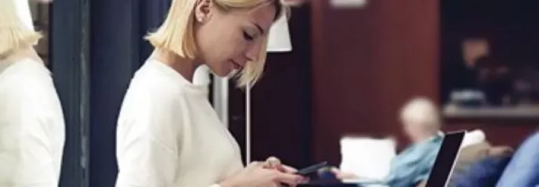 Person using a smartphone next to a laptop in a lounge.