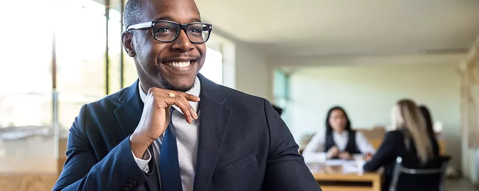 Person in a suit smiling in an office setting.