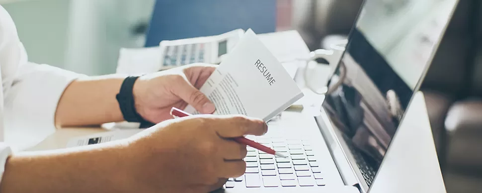 Person reviewing a resume at a desk with a laptop.
