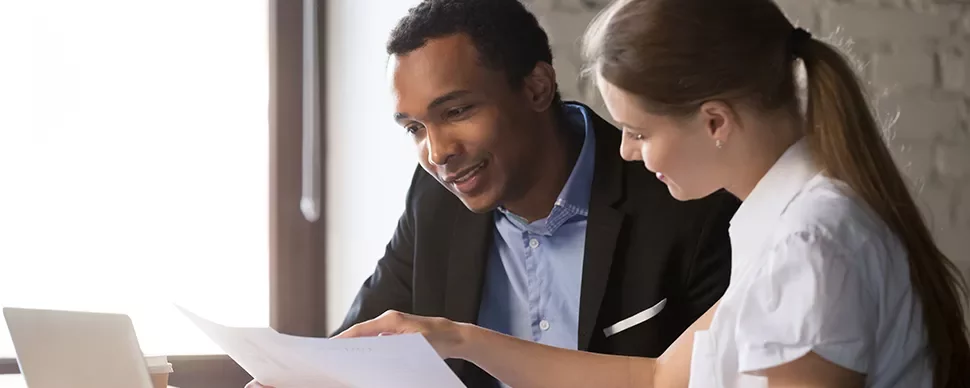 Deux personnes examinent un document sur un bureau avec un ordinateur portable.