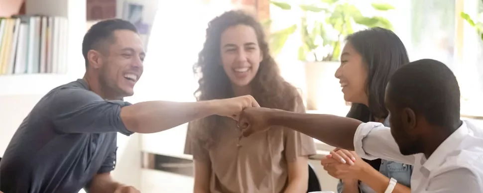 Groupe d'amis souriant et se cognant les poings autour d'une table.