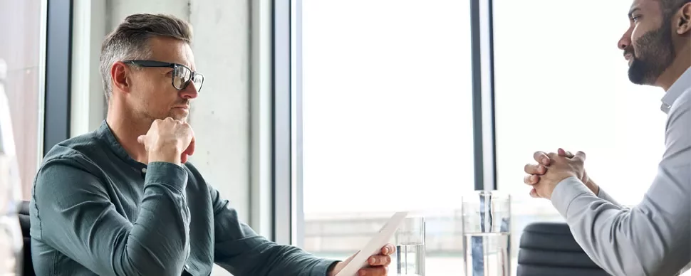 Deux personnes assises à une table, en train de converser près d'une fenêtre.