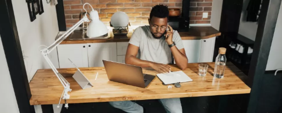 Person on the phone at a wooden desk with a laptop and notebook.