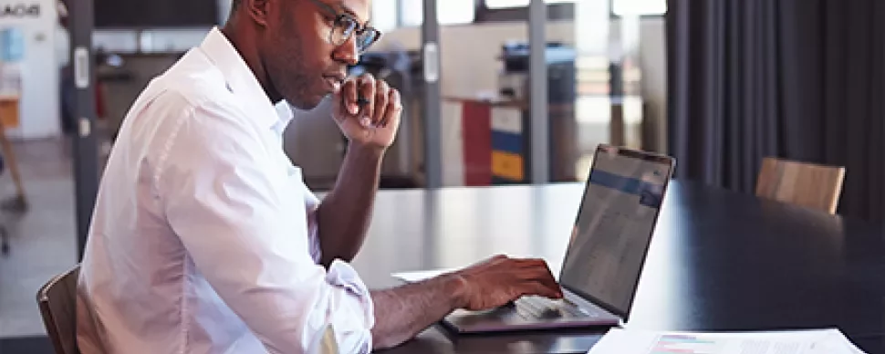 Personne travaillant sur un ordinateur portable à une table avec des documents.