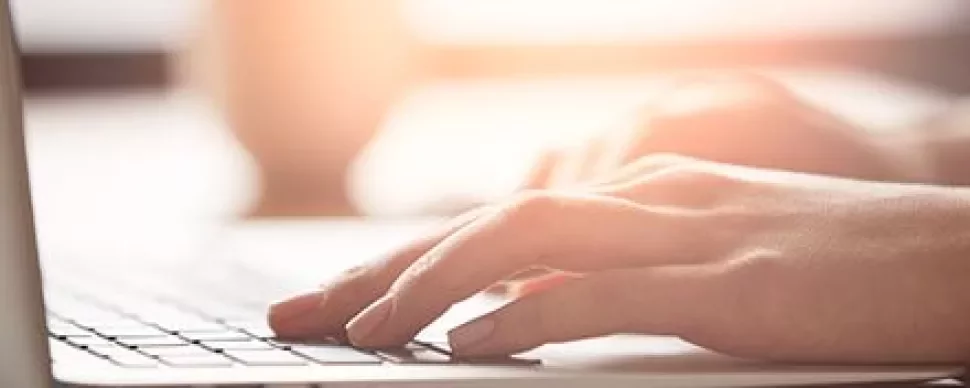 Mains tapant sur un clavier d'ordinateur portable en lumière douce.