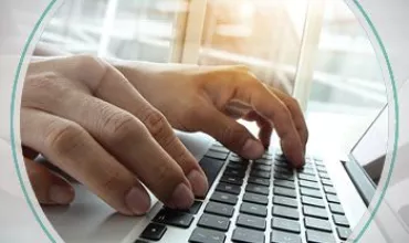 Hands typing on a laptop keyboard near a window.
