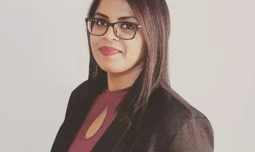 Person in glasses wearing a black jacket, smiling.