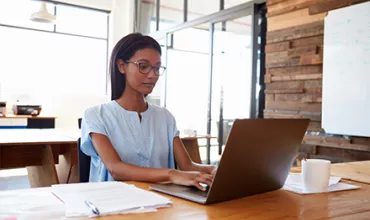 Person working on a laptop at a wooden desk in a modern office.