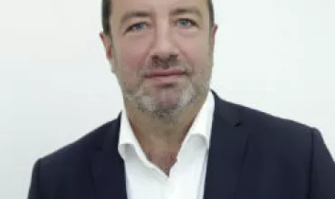 Person in a dark suit jacket and white shirt posing against a plain background.