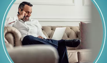 Personne assise sur un canapé utilisant un ordinateur portable et parlant au téléphone