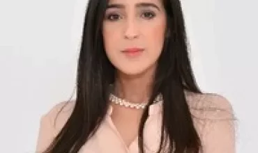 Personne aux cheveux longs portant une chemise beige, bras croisés.