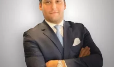 Personne en costume souriant avec les bras croisés.